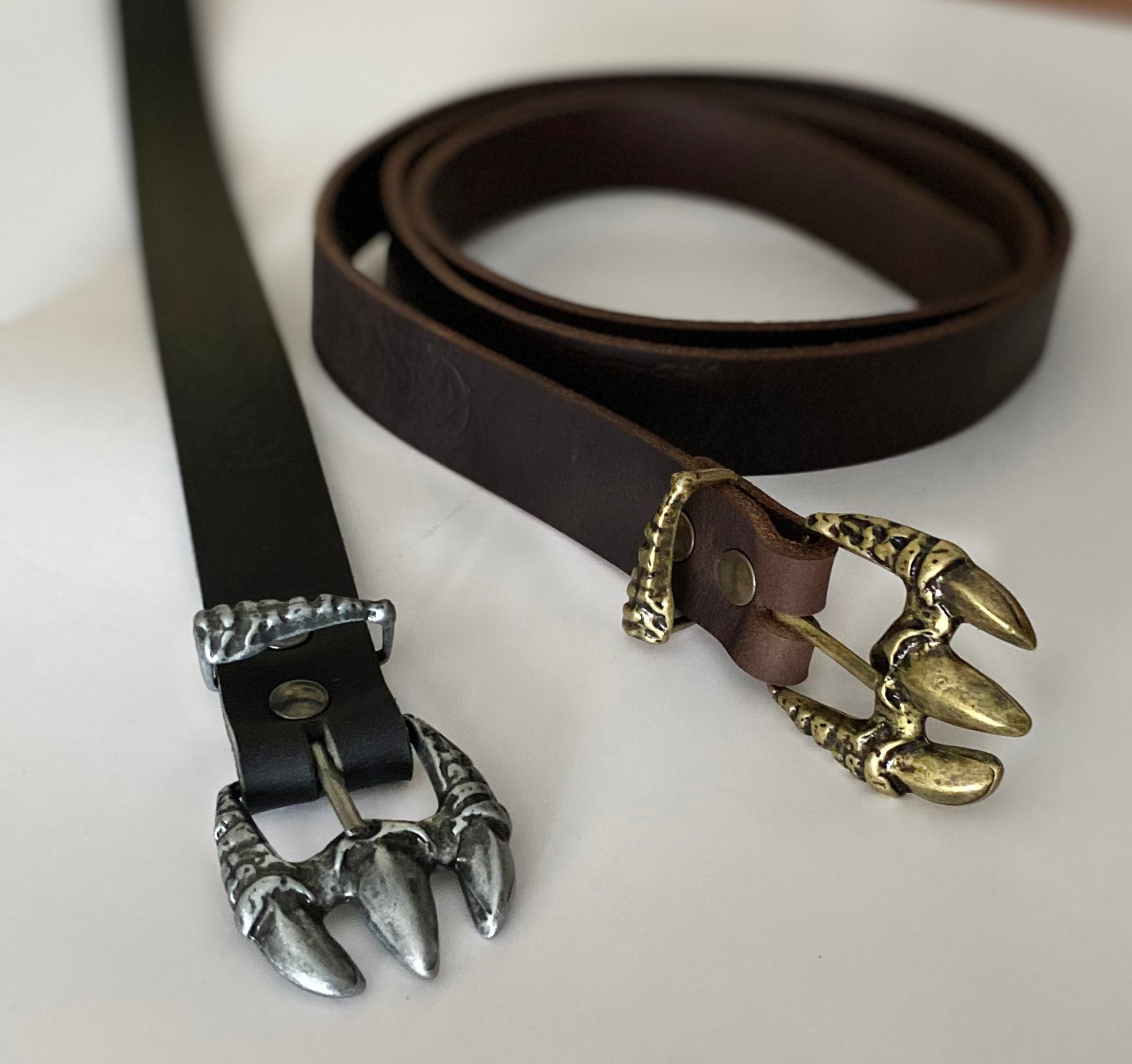 Ceinture Seyrawyn en cuir de couleur noir ou brun, avec une boucle en métal en forme de patte de dragon.